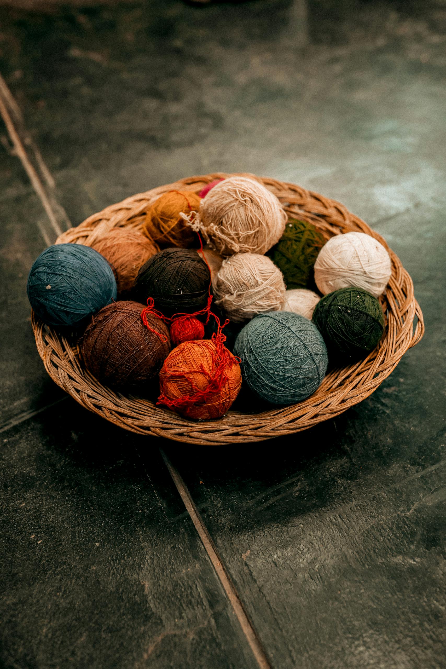 A variety of colorful yarn balls neatly arranged in a wicker basket on a dark surface.