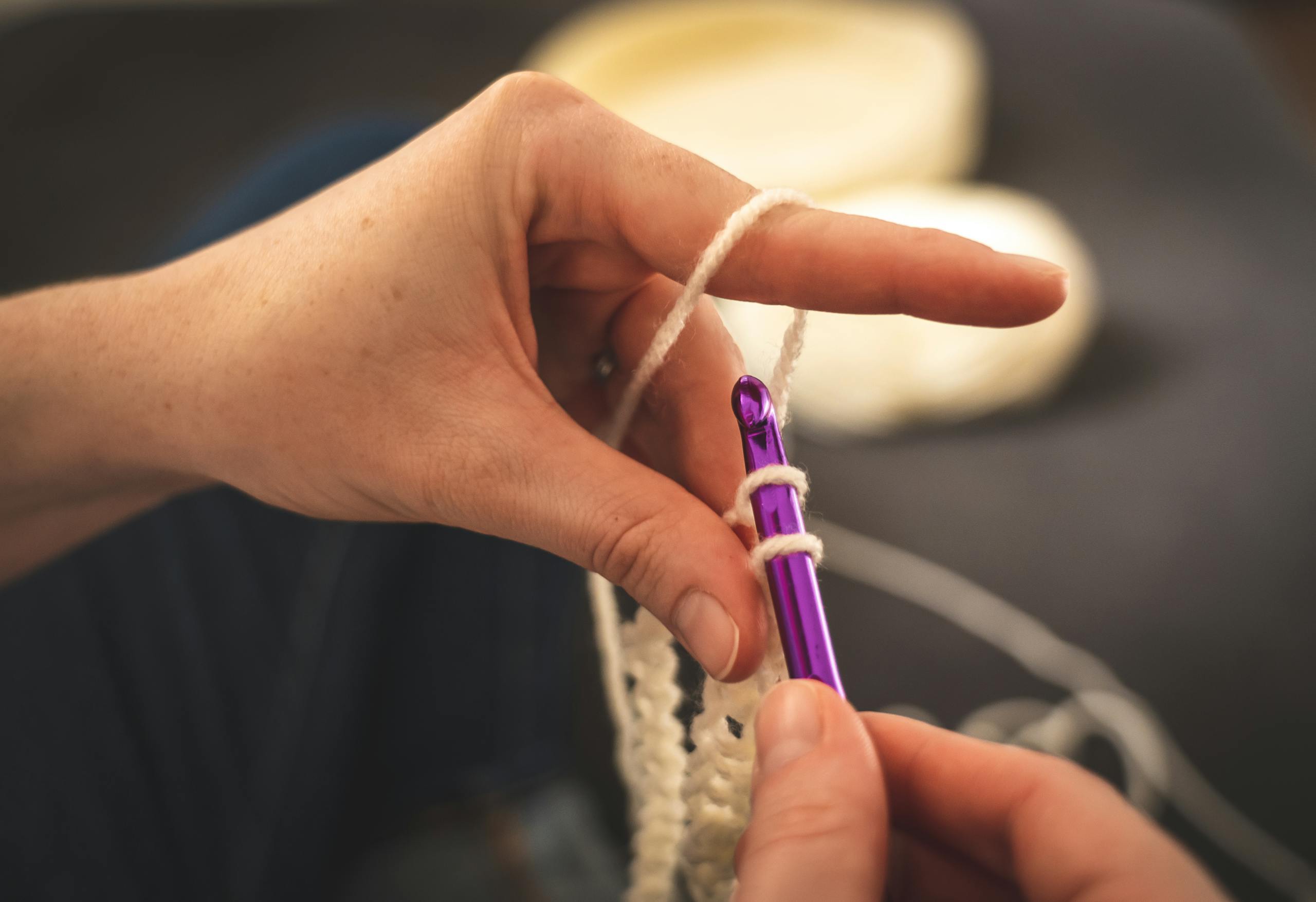 Detailed view of hands crocheting with a purple hook, highlighting the handmade craft process.