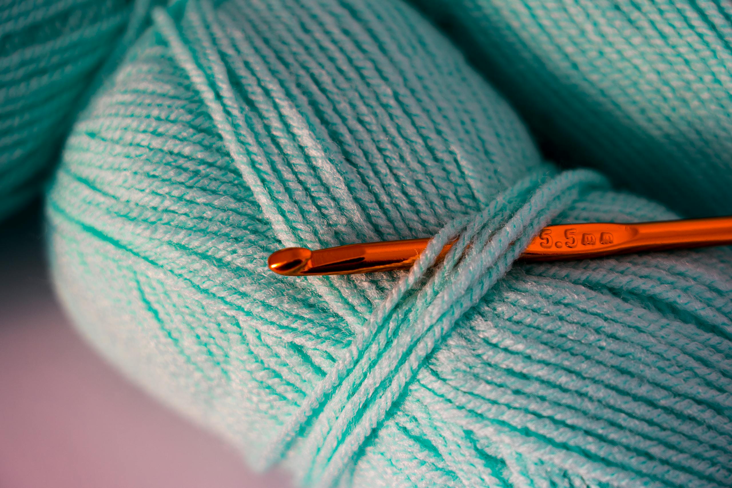 Macro photograph of teal yarn with a crochet hook, highlighting texture and detail.